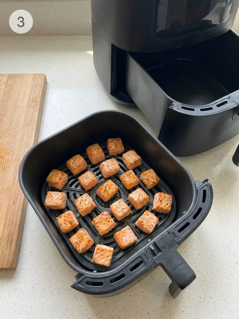 Seasoned salmon cubes with lightly browned edges spaced in a single layer in an air fryer basket